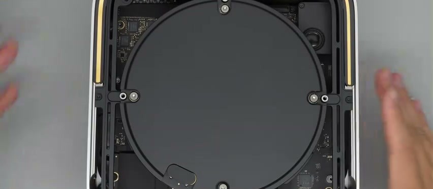 Mac Studio M5 aperto dal fondo: il coperchio rotondo dell'alimentatore fissato con viti dentro il guscio in alluminio